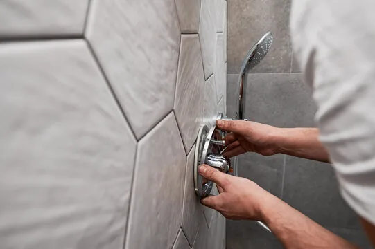 Plumber installing a shower mixing valve trim on a tiled bathroom wall