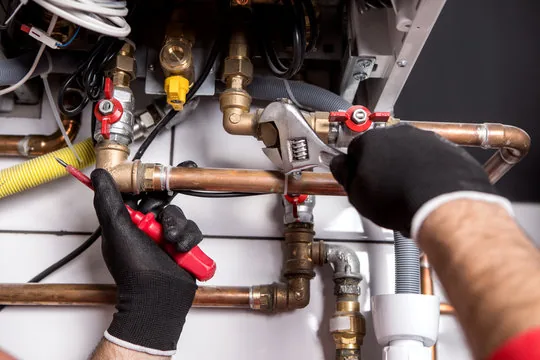 Plumber tightening copper fittings and valves on a water heater with a wrench